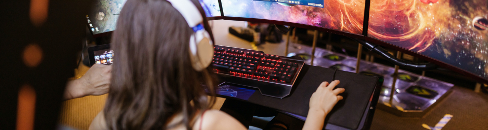 Uma jovem usando headphone joga um jogo em um computador com diversas telas