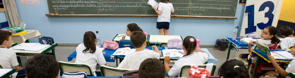 Uma sala de aula com diversos estudantes e um deles está escrevendo em um quadro negro