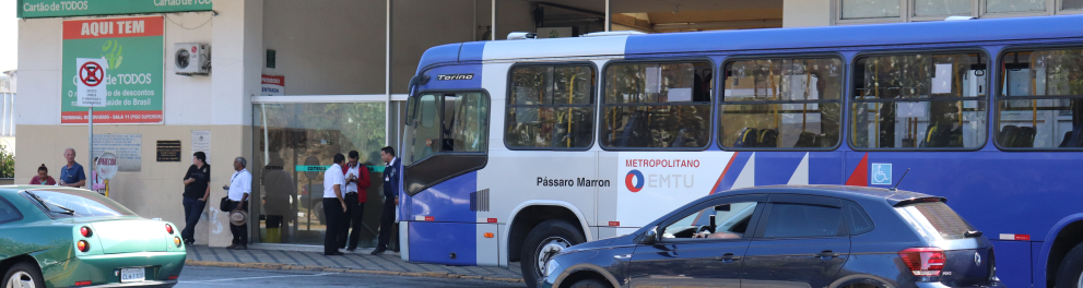 Imagem da fachada de uma rodoviária brasileira com um ônibus azul e branco estacionado à frente e carros passando na rua