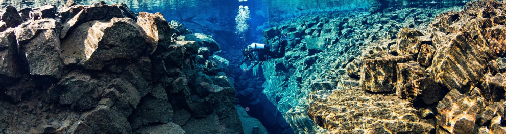 Imagem subaquática de um mergulhador nadando entre rochas submersas bem grandes