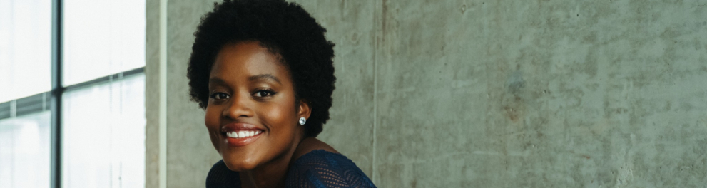 Mulher negra está sorridente para quem bateu a foto e apoiada em um corremão