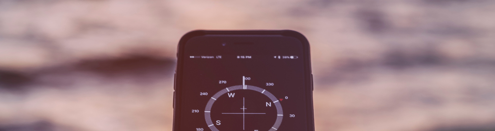 Imagem da mão esquerda de um homem branco segurando um celular que está apontado para o mar e marcando um um número que parece ser relacionado ao vento ou às correntezas