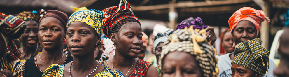 Mulheres africanas com roupas coloridas características de sua cultura estão em pé e de frente para quem bateu a foto
