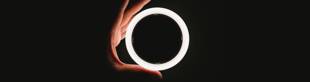 Uma lâmpada fluorescente circular está sendo segurada pela mão esquerda de alguém sobre um fundo totalmente escuro