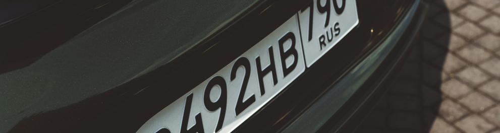 Close na parte traseira de um carro preto mostrando a placa russa e a marca Porsche