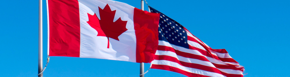 Bandeiras de Canadá e Estados Unidos lado a lado penduradas em mastros verticais