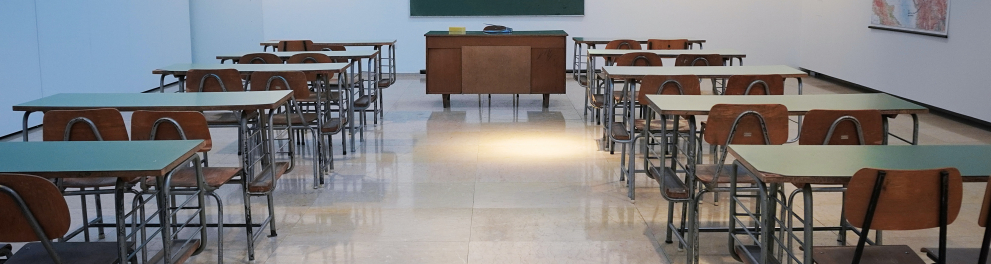 Uma sala de aula vazia, apenas com as cadeiras, a mesa do professor e o quadro negro em branco ao fundo