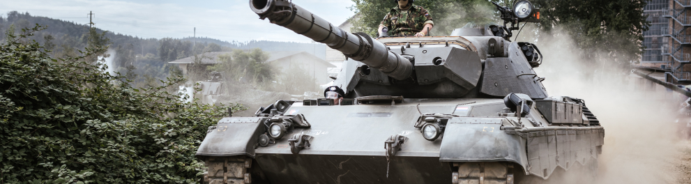 Um tanque de guerra está de frente para quem bateu a foto e está em movimento com um soldado no topo