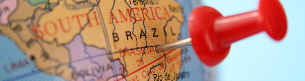 Um mapa mundi de um globo azul está closado no Brasil, que ainda tem um alfinete vermelho espetado em seu centro
