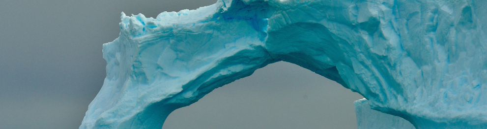 Um bote inflável com algumas pessoas muito agasalhadas está navegando em um mar gélido da Antártida e está se aproximando de uma espécie de iceberg com uma abertura