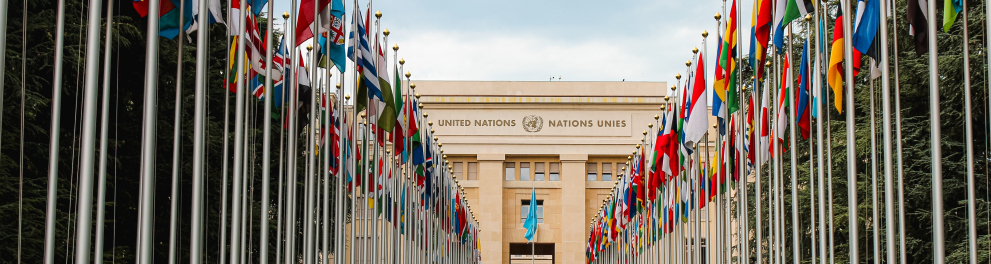 Fachada do prédio da ONU em Genebra, com as bandeiras dos países posicionadas no jardim formando um corredor