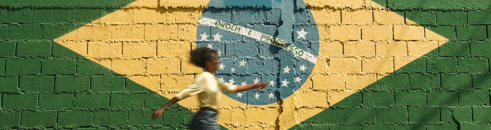 Uma mulher de perfil para quem bateu a foto está andando em frente a um muro que tem a bandeira do Brasil pintada