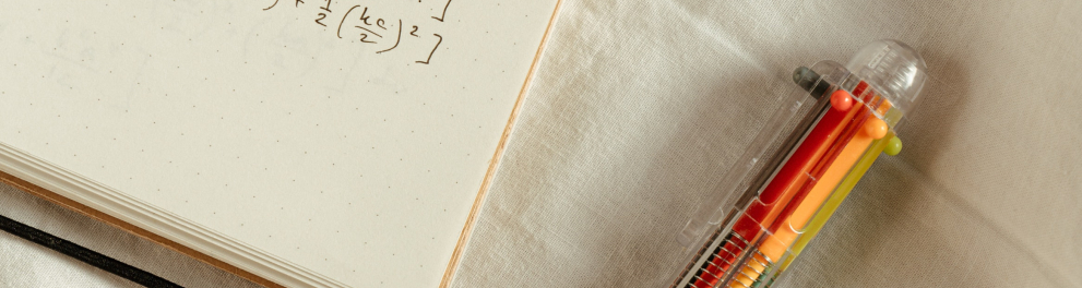 Parte de um caderno com anotações sobre matemática e uma caneta de cor laranja ao lado
