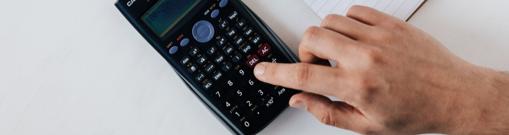 Uma pessoa fazendo cálculos em uma calculadora, com um caderno e cédulas de dólar ao lado