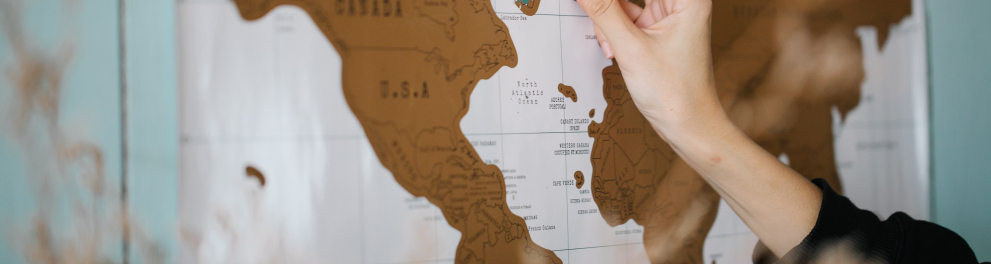 Mão direita de uma mulher branca está inserindo uma peça em um mapa mundi. As Américas estão mais à mostra no mapa