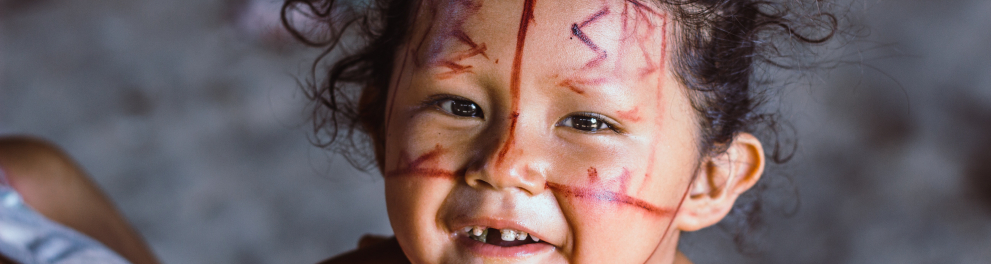 Uma menina está com o rosto pintado com a cultura indígena e tinta vermelha