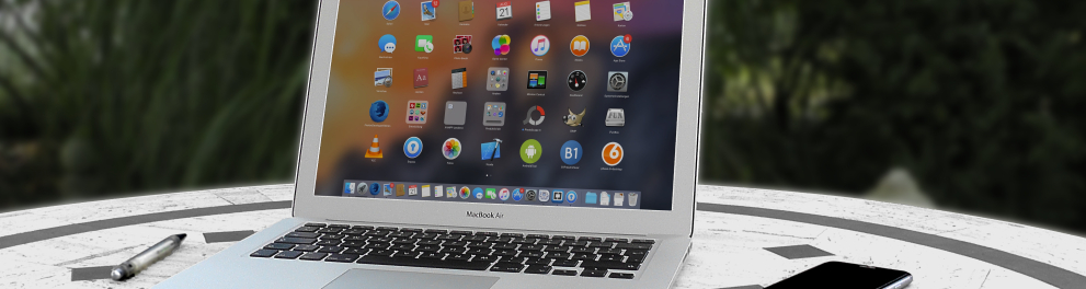 Um notebook aberto mostrando o ícone de vários apps em sua tela está em cima de uma mesa junto de um celular e uma caneta