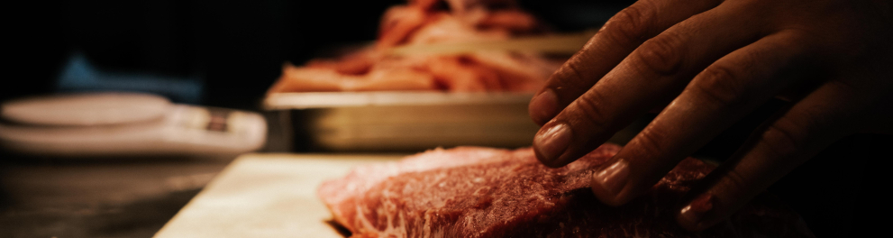 Uma carne vermelha ainda crua sendo fatiada em cima de uma tábua de madeira