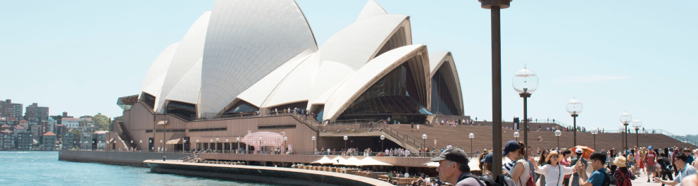 Várias pessoas  em frente a um ponto turístico da Austrália, o teatro Ópera de Sydney