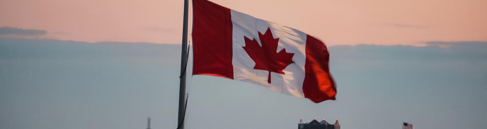 Uma bandeira do Canadá erguida sobre um mastro e, ao fundo, podemos ver uma cidade