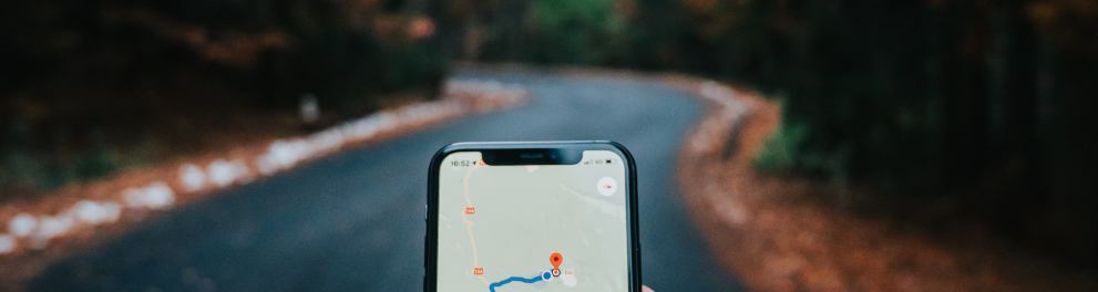 Imagem da mão esquerda de um homem branco segurando um celular, que mostra um mapa GPS na tela