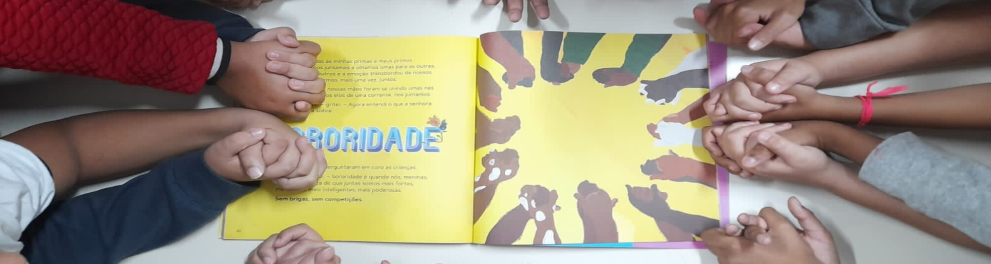 Crianças dão as mãos sobre livro escrito "Sororidade"