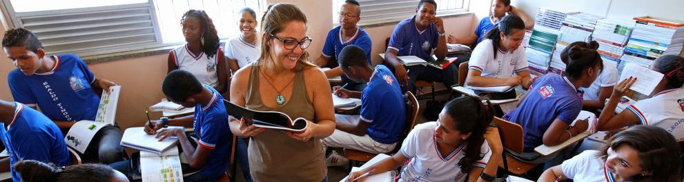Uma sala de aula com a professora no centro da sala