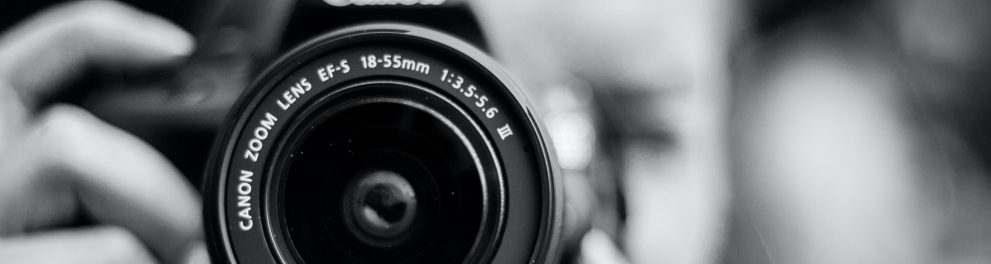 Imagem em close e em preto e branco de uma máquina fotográfica sendo utilizada por uma mulher