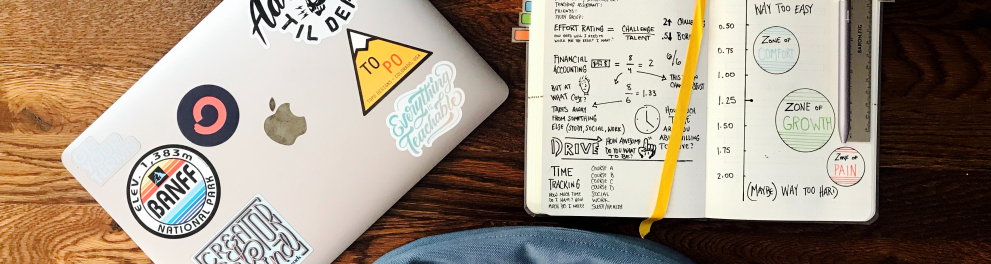 Imagem de uma mochila, um caderno aberto com anotações de matemática e um notebook fechado sobre uma superfície de madeira, que parece ser uma mesa