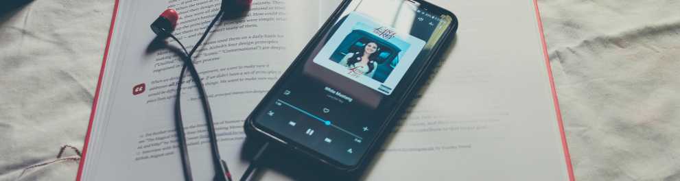 Um celular conectado em um app de músicas e com fones de ouvido plugado está em cima de um livro aberto