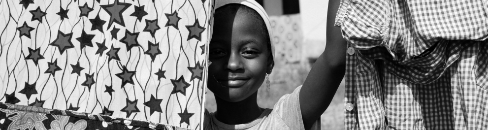Uma criança negra sorrindo em meio a um varal de roupas