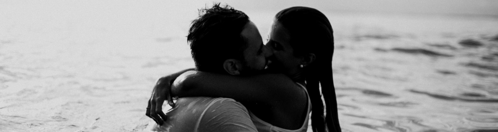 Um casal está abraçado enquanto se beija, dentro do mar.