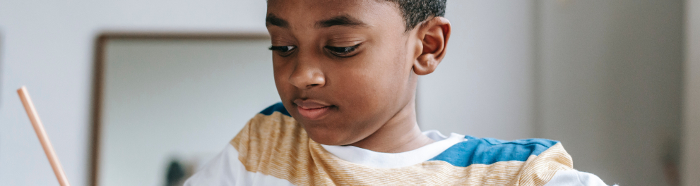Um jovem menino negro está escrevendo algo em um caderno