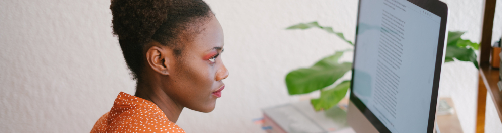 Uma mulher negra está escrevendo diante da tela de um computador de mesa.