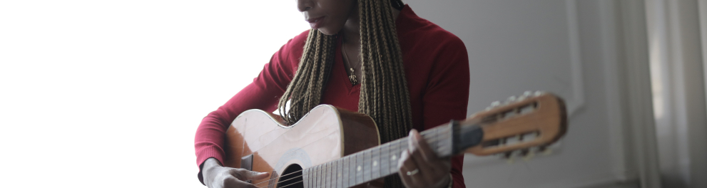 Uma mulher negra, de cabelo comprido, toca violão.