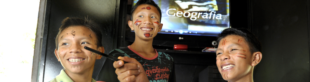 Jovens indígenas sorriem em uma sala de aula do Telecurso, com uma tv.