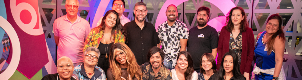 Diversas pessoas reunidas em uma sala com fundo em tons de roxo.