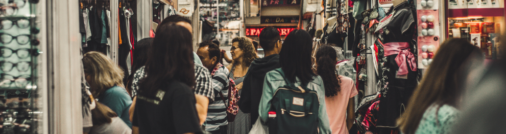 Foto do que parece ser o interior de uma galeria ou shopping, onde há várias pessoas e lojas com placas