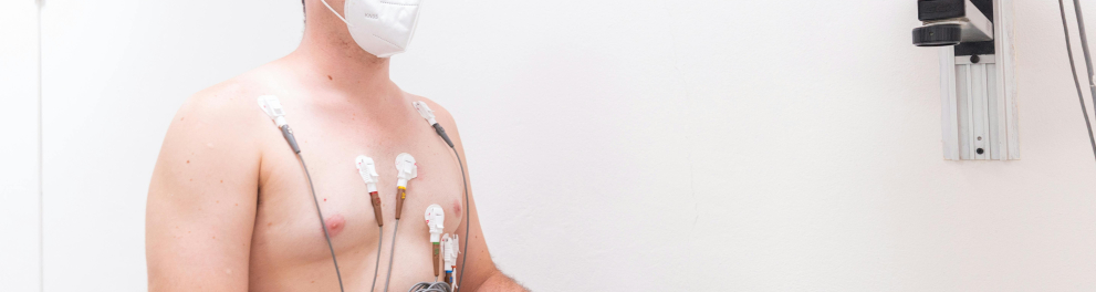 Um homem branco sem camisa está em uma esteira fazendo testes físicos, pois ele está cheio de eletrodos pelo tronco e uma máscara