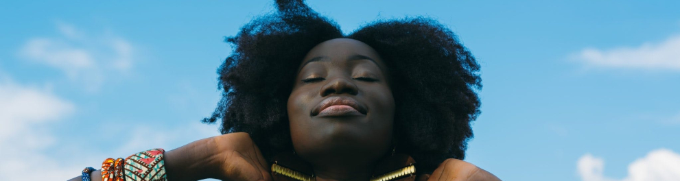 Uma mulher negra sorrindo de olhos fechados e com as mãos no cabelo