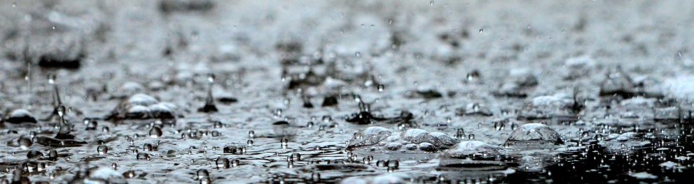 Imagem de pingos de chuva caindo sobre poça d'água à noite