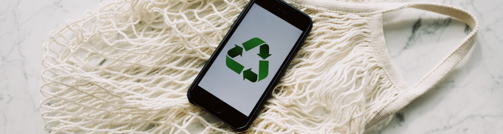 Um celular com a tela mostrando o símbolo verde da sustentabilidade está em cima de uma sacola de lã branca
