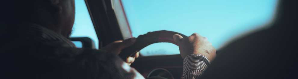 Imagem feita dentro de um automóvel por algum passageiro no banco de trás mostra um homem dirigindo o veículo, com as duas mãos no volante