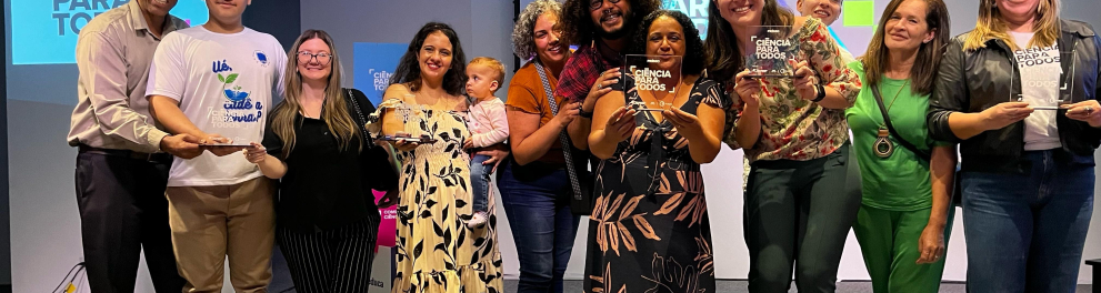 Várias pessoas lado lado em um palanque posando para quem bateu a foto e exibindo troféus escritos Ciência Para Todos