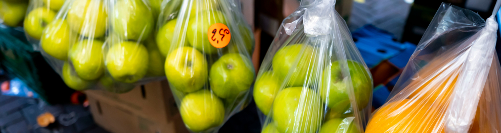Maçãs verdes e laranjas embrulhadas em sacos plásticos