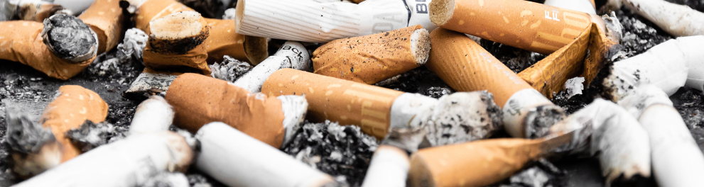 Várias guimbas de cigarro estão espalhadas pelo chão, que parece ser asfalto ao ar livre