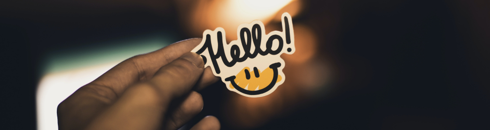 Mão esquerda de uma pessoa está segurando um adesivo brilhante em meio ao escuro com a palavra "Hello"