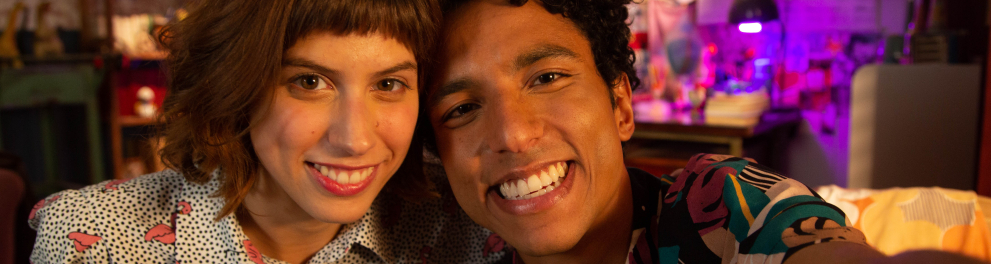 Uma mulher e um homem estão sentados em um sofá. Ambos sorriem.