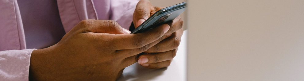 Mulher preta usando o celular enquando está de frente para uma tela de computador.