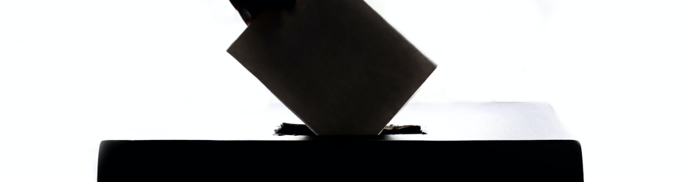 Uma mão depositando um voto em uma urna.